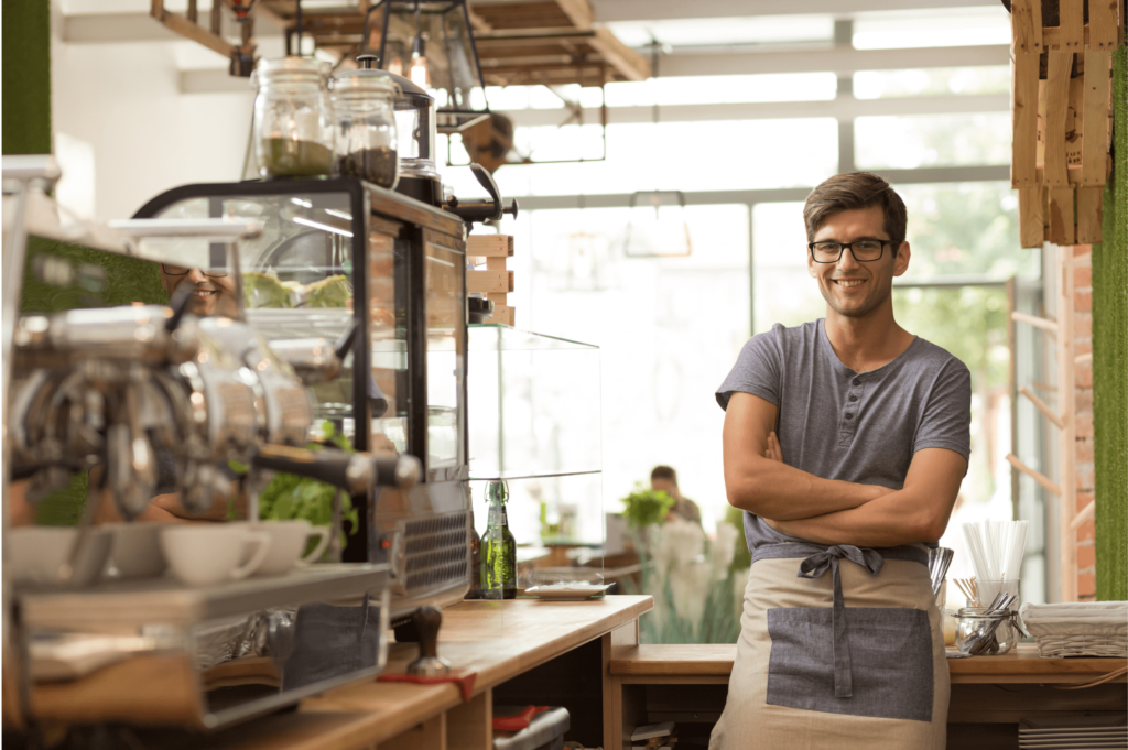 Confident young male cafe owner with arms crossed in his coffee shop