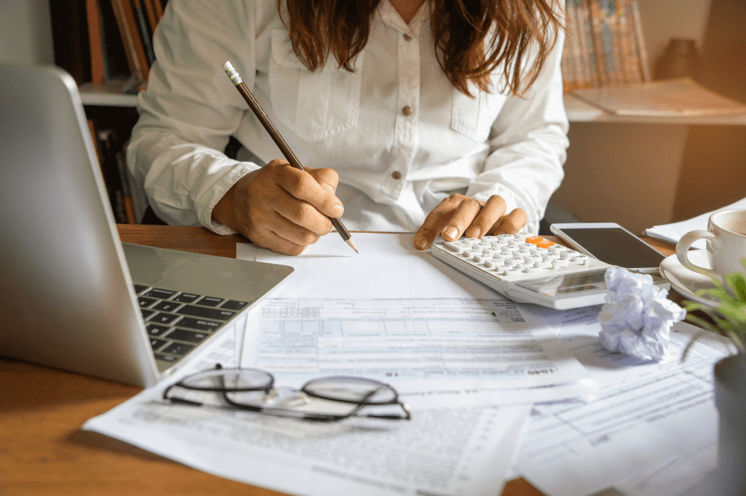 Person calculating budget using a calculator and filling out financial forms, symbolizing the costs involved in promoting a website on Google.